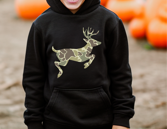 Child wearing Camo Deer Youth Hoodie with a camouflage deer silhouette, standing in an outdoor autumn setting with pumpkins visible in the background.