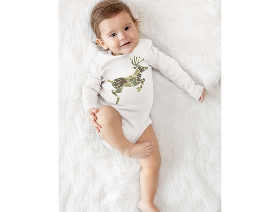 Baby in Camo Deer Long Sleeve Onesie on white furry surface, smiling, showcasing the onesie's camouflage deer graphic and durable design features.