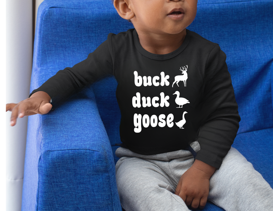 Child wearing Buck, Duck, Goose, Toddler Long Sleeve Tee with playful animal graphics, seated on a blue chair, paired with gray sweatpants.