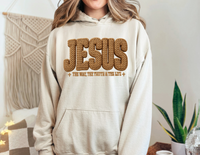 Person wearing a beige Jesus Hoodie with The Way, The Truth & The Life text, featuring a kangaroo pocket and matching drawstring, in a cozy setting.