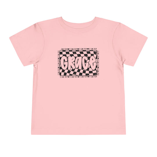 Grace Toddler Tee featuring a playful black and white text design on a pink shirt, perfect for kids' everyday comfort with its soft cotton fabric.