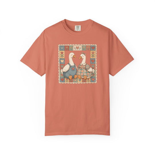 Thrifted Geese Tee: Salmon-toned T-shirt featuring folk-art geese in heart and tulip frame. Comfortable, garment-dyed cotton, relaxed fit, and durable stitching for everyday wear.
