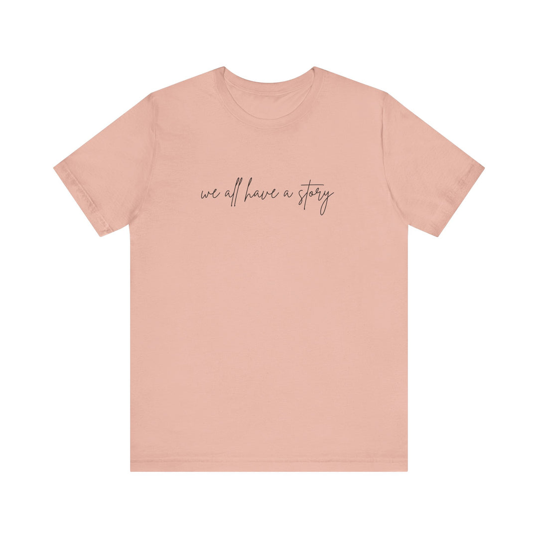 We all have a Story Tee with black text on a pink background, showcasing a comfortable unisex fit perfect for casual wear.