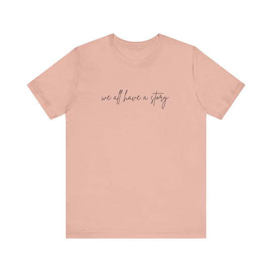 We all have a Story Tee with black text on a pink background, showcasing a comfortable unisex fit perfect for casual wear.