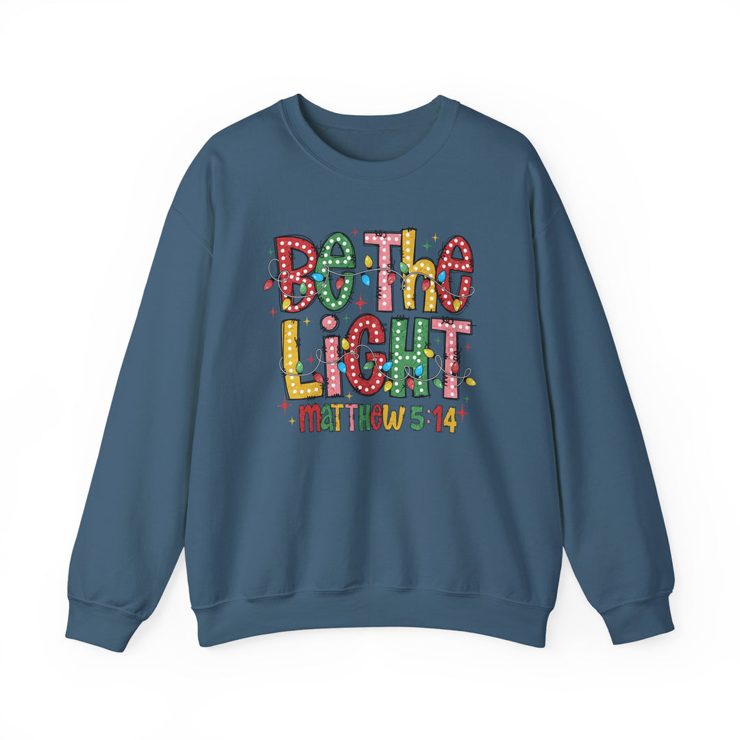 Teal-blue crewneck sweatshirt featuring Be the Light in Christmas-lights motif with Matthew 5:14 beneath, offering comfort and durability.