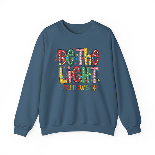 Teal-blue crewneck sweatshirt featuring Be the Light in Christmas-lights motif with Matthew 5:14 beneath, offering comfort and durability.