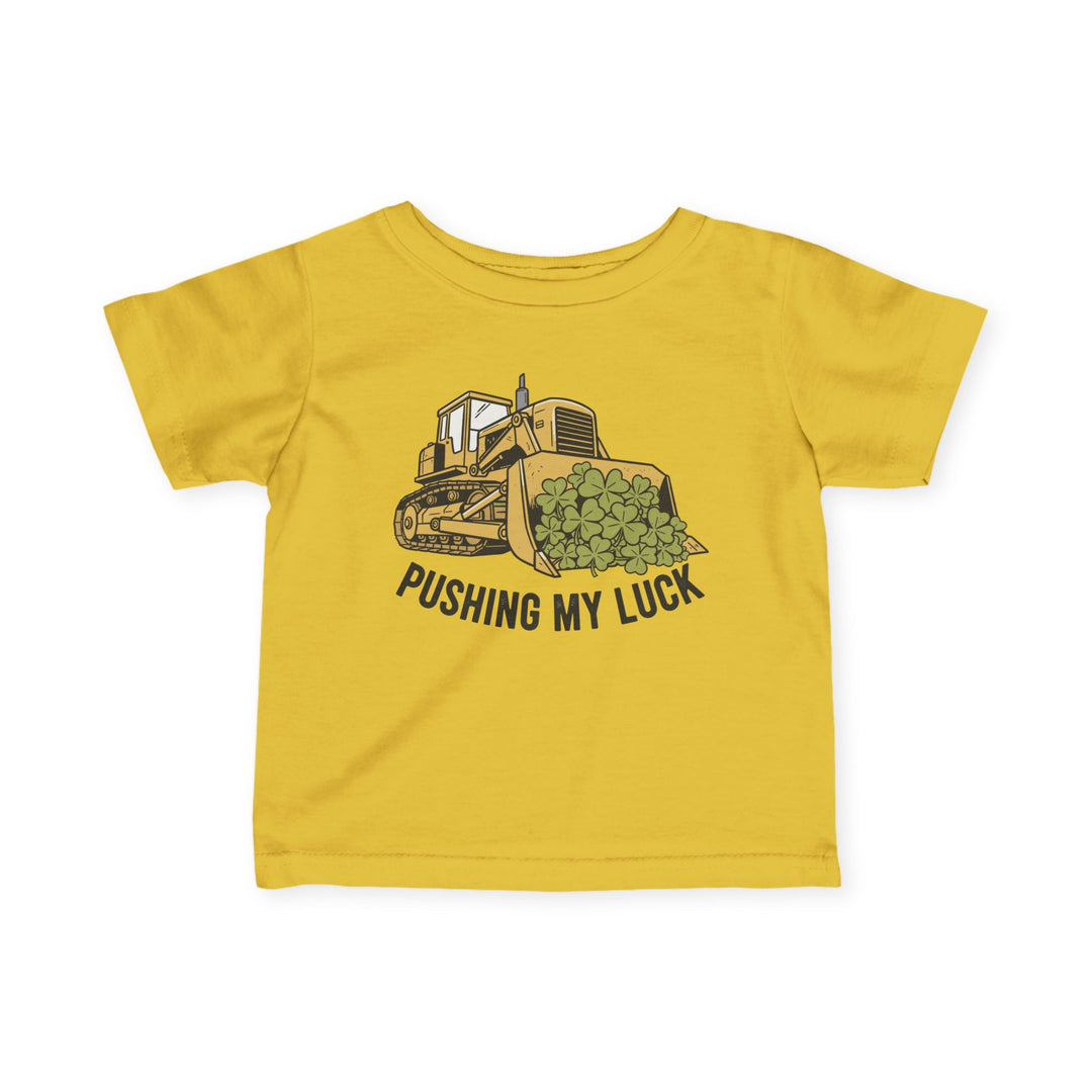 Pushing My Luck Baby Tee: Bright yellow kids' T-shirt with a cartoon bulldozer carrying clover, slogan PUSHING MY LUCK, offering comfort and durability for toddlers.