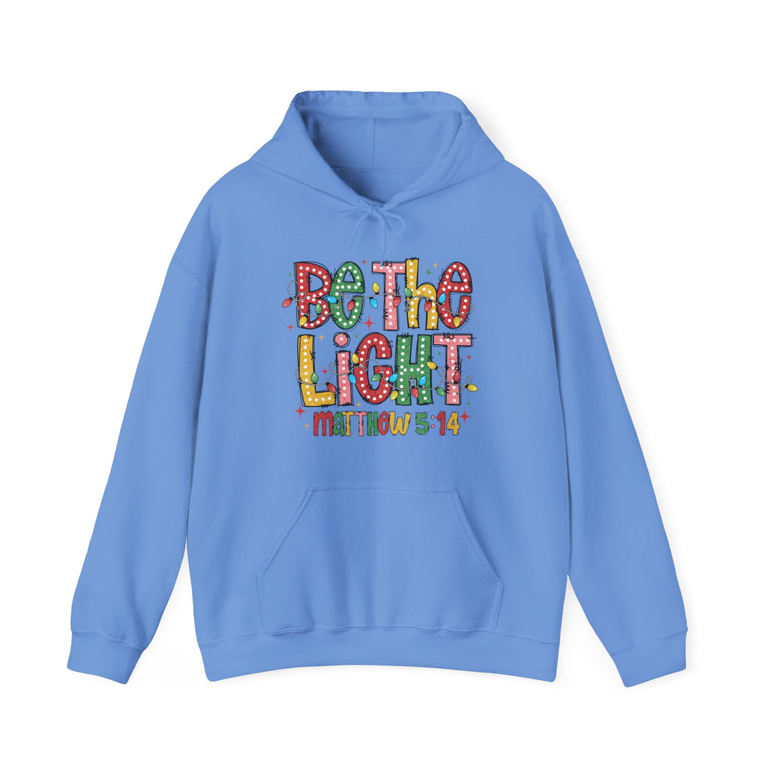 Light-blue Be the Light hoodie with festive Christmas lights design, kangaroo pocket, and drawstring hood, offering cozy warmth and style for cold days.