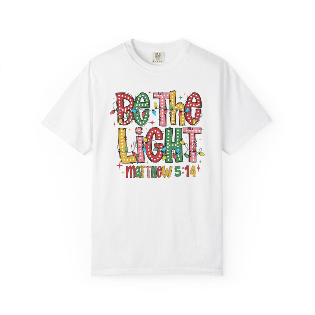 Be the Light Tee featuring Christmas light-themed 'BE THE LIGHT' graphic and 'Matthew 5:14' on a white short-sleeve shirt.