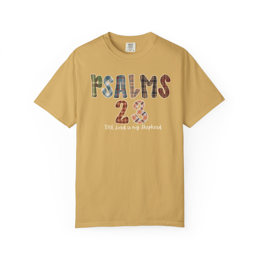 Mustard-yellow Psalms 23 T-shirt with plaid-patterned lettering, reading The Lord is my Shepherd, from Faith Family Designs. Various sizes available for a relaxed fit.
