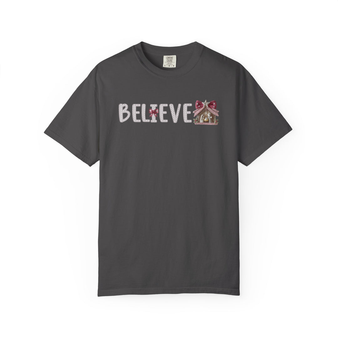 Charcoal-gray Believe Tee with BELIEVE in white font, featuring red bows, stripes, and a gingerbread house graphic on the chest.
