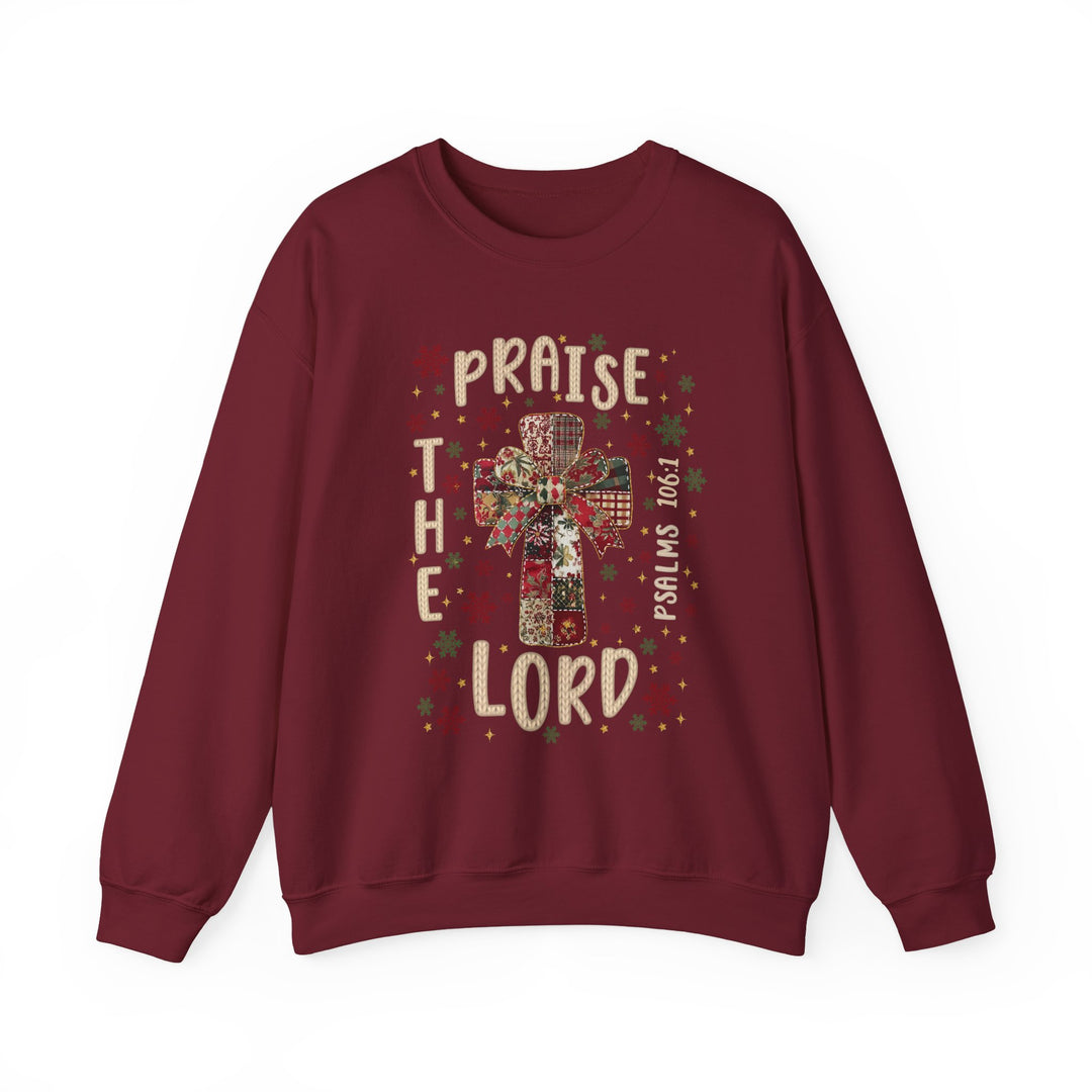 Maroon sweatshirt with festive cross and bow design, featuring PRAISE THE LORD and Psalms 106:1, surrounded by star and snowflake motifs.