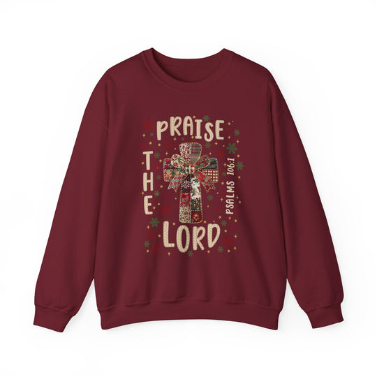 Maroon sweatshirt with festive cross and bow design, featuring PRAISE THE LORD and Psalms 106:1, surrounded by star and snowflake motifs.