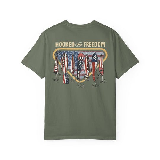 Back view of the Hooked on Freedom Tee, showcasing a fishing motif with patriotic lures against a flag-inspired backdrop on an olive-green Comfort Colors T-shirt.