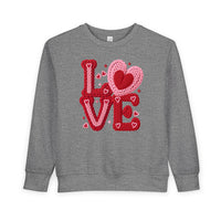 Heather-gray toddler sweatshirt with LOVE in chunky red and pink knitted-yarn letters, featuring hearts, from Faith Family Designs. Cozy and durable for Valentine's theme.
