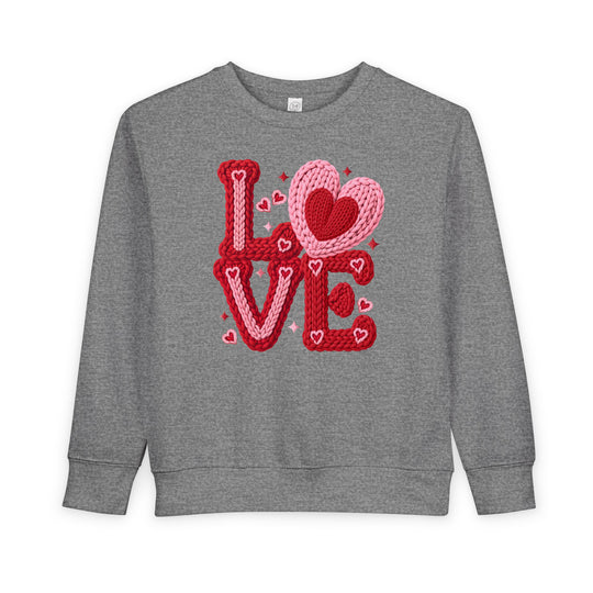 Heather-gray toddler sweatshirt with LOVE in chunky red and pink knitted-yarn letters, featuring hearts, from Faith Family Designs. Cozy and durable for Valentine's theme.