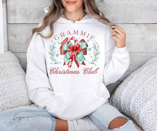 Person wearing a Grammie Christmas Club hoodie with candy cane design, seated with cozy knit accessories, embodying festive and comfortable style.