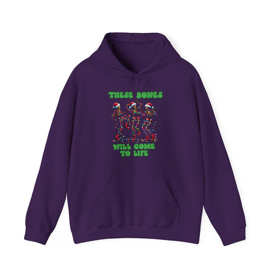 Purple hoodie featuring three Santa-hat-wearing skeletons with holiday lights, captioned “THESE BONES WILL COME TO LIFE,” includes kangaroo pocket and drawstring hood.