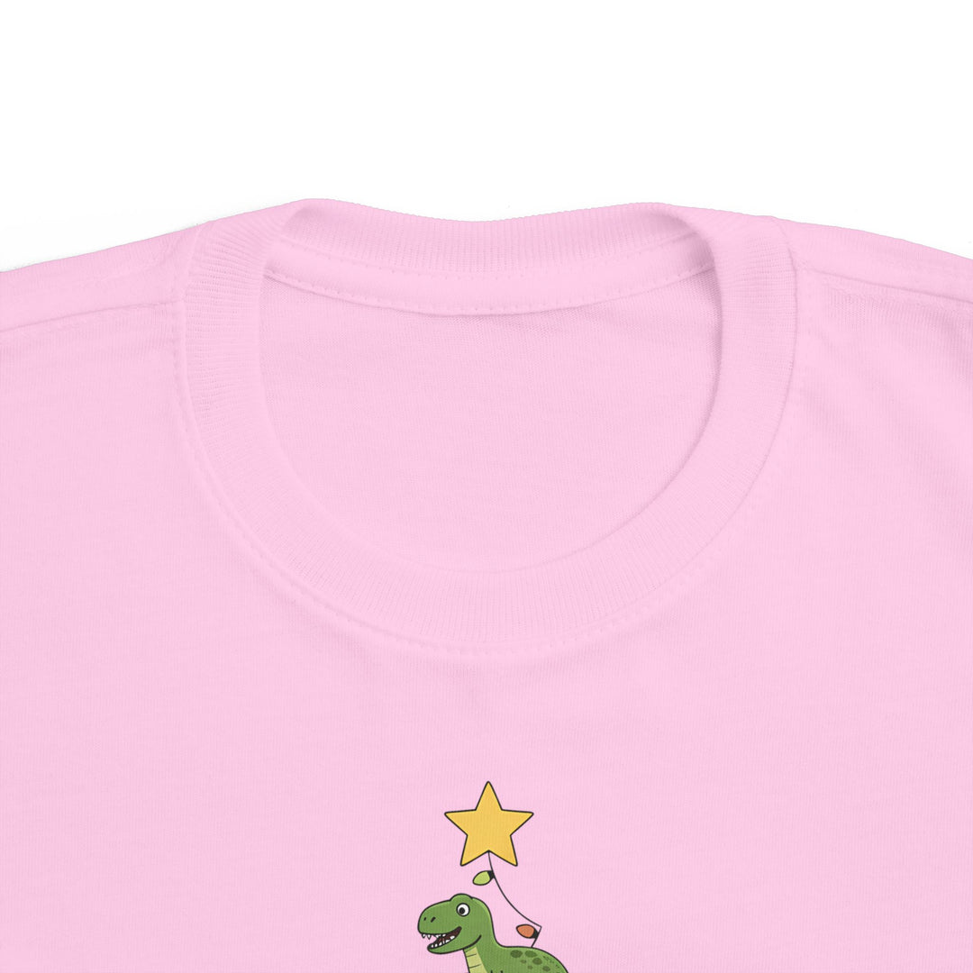 Dino Tree Toddler Tee featuring a cartoon green dinosaur with a star on a light pink shirt, perfect for toddlers' sensitive skin.