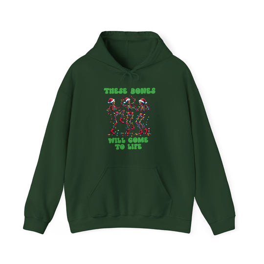 Dark-green hoodie with three dancing skeletons in Santa hats, wrapped in Christmas lights. Text reads THESE BONES WILL COME TO LIFE, referencing Ezekiel 37:1-5.