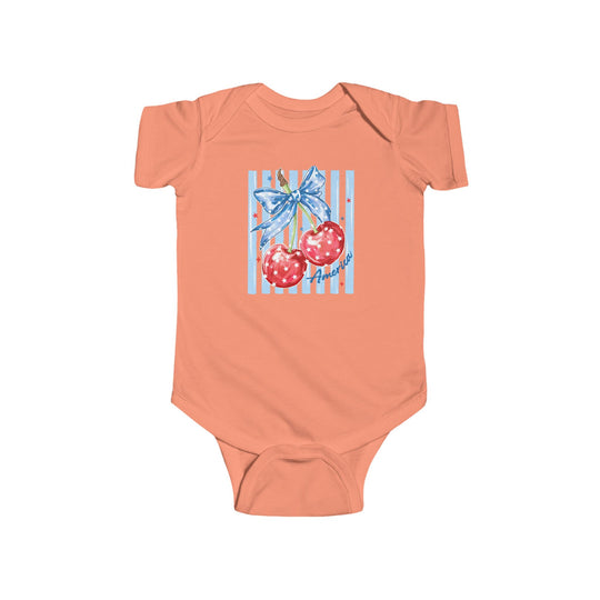 American Cherry Onesie: Soft coral baby bodysuit featuring cherries with a blue star ribbon and America script, ensuring comfort with durable cotton and convenient snap closures.