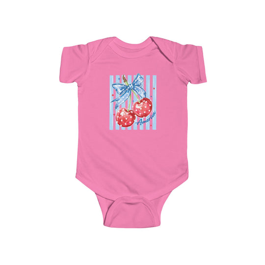 American Cherry Onesie: Pink infant bodysuit featuring glossy cherries with a blue ribbon, pale blue stripes, and America in cursive. Durable cotton, easy-snap closure.