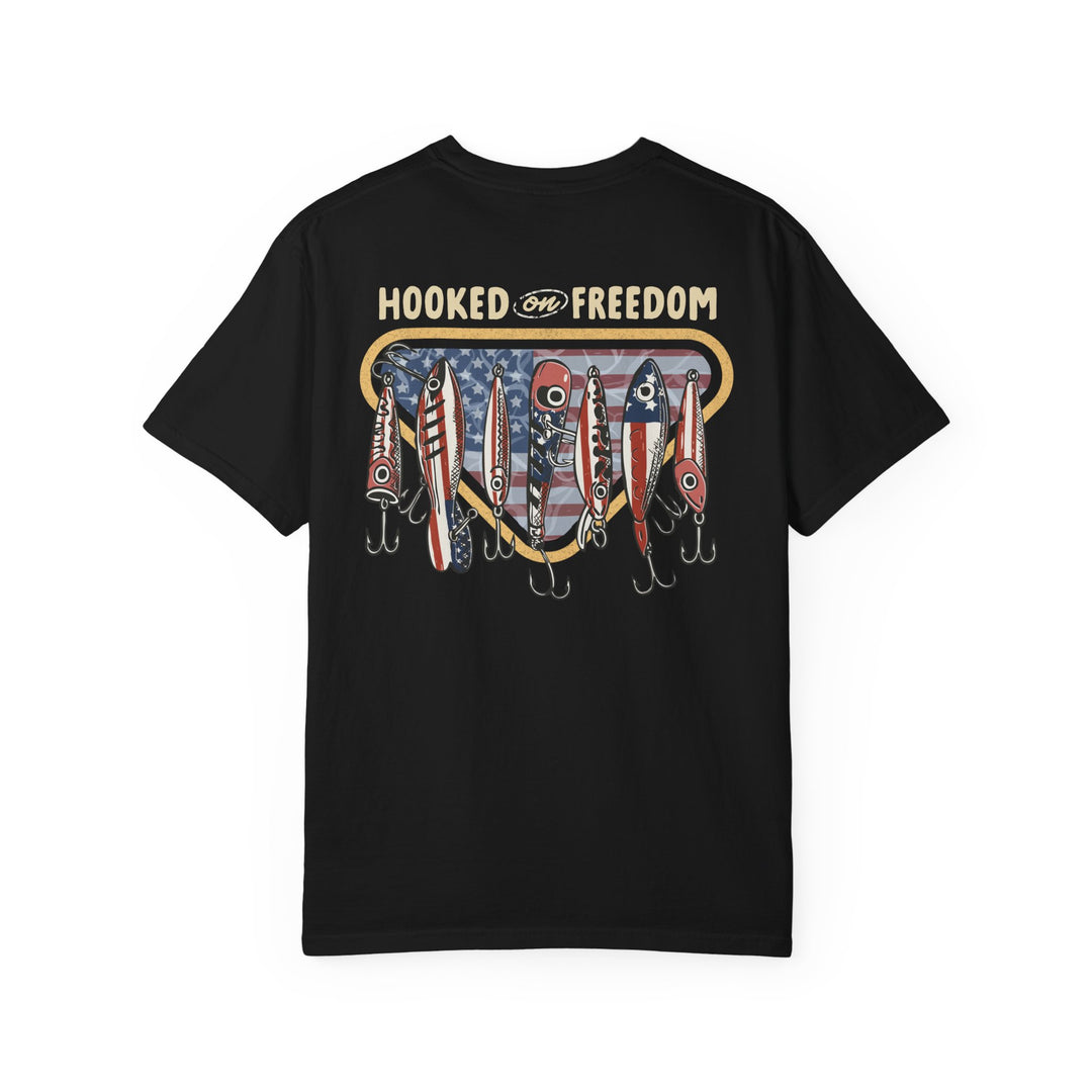 Hooked on Freedom Tee featuring a patriotic fishing theme with slogan and American flag emblem, accented by red, white, and blue fishing lures.