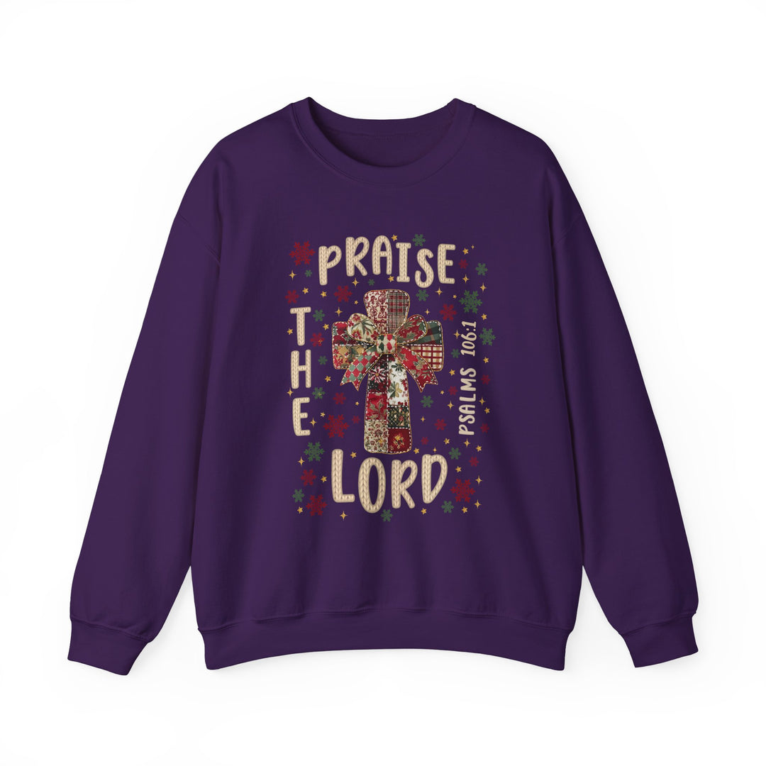 Purple crew-neck sweatshirt featuring a quilt-patterned cross with a bow, stars, snowflakes, and the words “Praise the Lord” and “Psalms 106:1.”