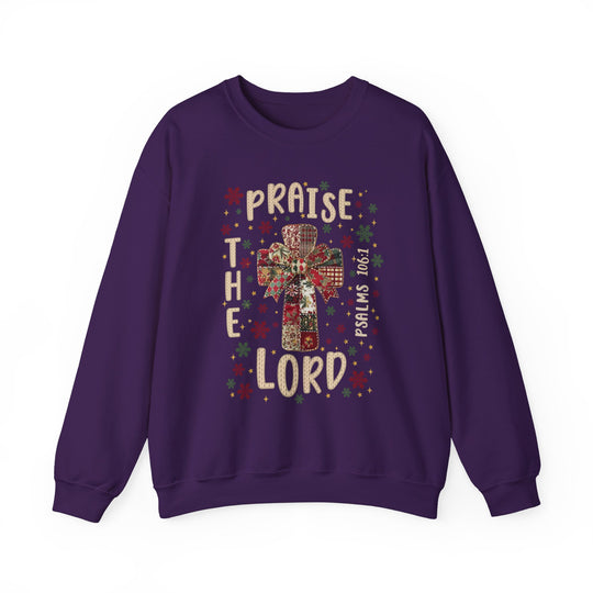 Purple crew-neck sweatshirt featuring a quilt-patterned cross with a bow, stars, snowflakes, and the words “Praise the Lord” and “Psalms 106:1.”