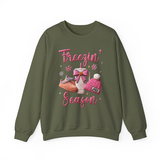 Freezin Season Crew: Olive-green sweatshirt with winter-themed embroidery, featuring Freezin’ Season text, slippers, a cup, beanie, snowflakes, and sparkles. Cozy, unisex, and comfortable fit.