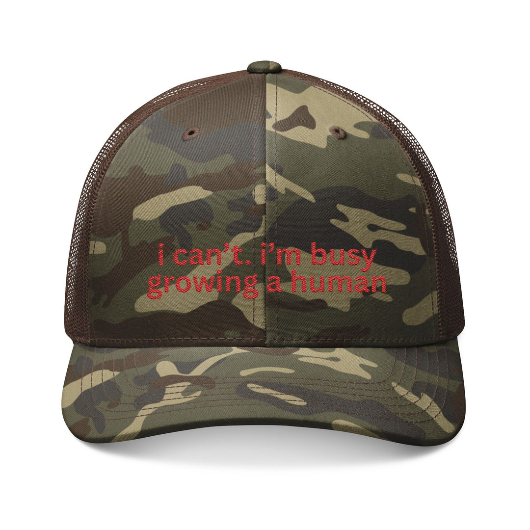 Camouflage-patterned trucker hat with red embroidery reading i can’t. i’m busy growing a human. Features mesh back and adjustable snap closure for comfort.