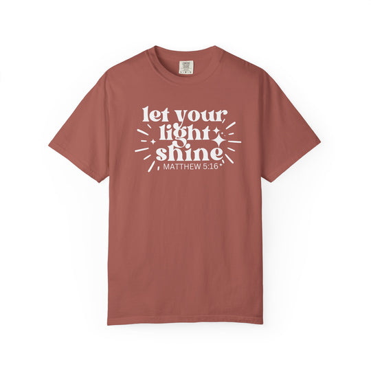Unisex rust-colored crew-neck T-shirt with let your light shine MATTHEW 5:16 in bold white font, featuring spark-and-ray graphics around light.