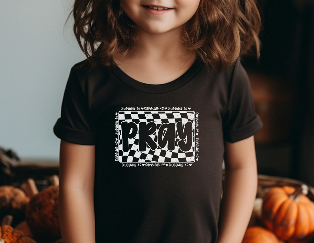Toddler wearing a black Pray Toddler Tee stands in front of pumpkins, illustrating the playful and comfortable style of Worlds Worst Tees' unique kids' collection.