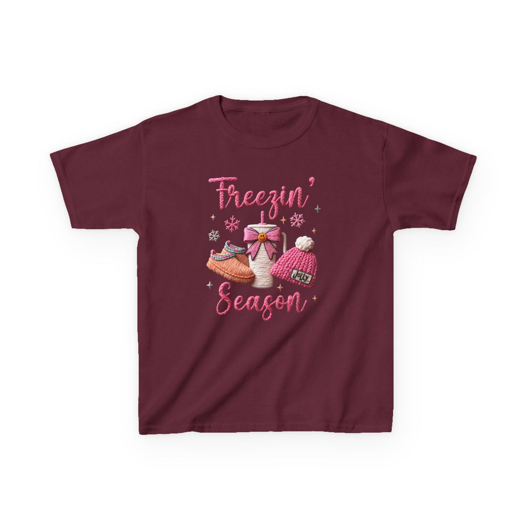 Freezin Season Kids Tee featuring playful winter-themed embroidery with a steaming thermos, cozy slippers, pom-pom beanie, and snowflakes on a maroon backdrop.