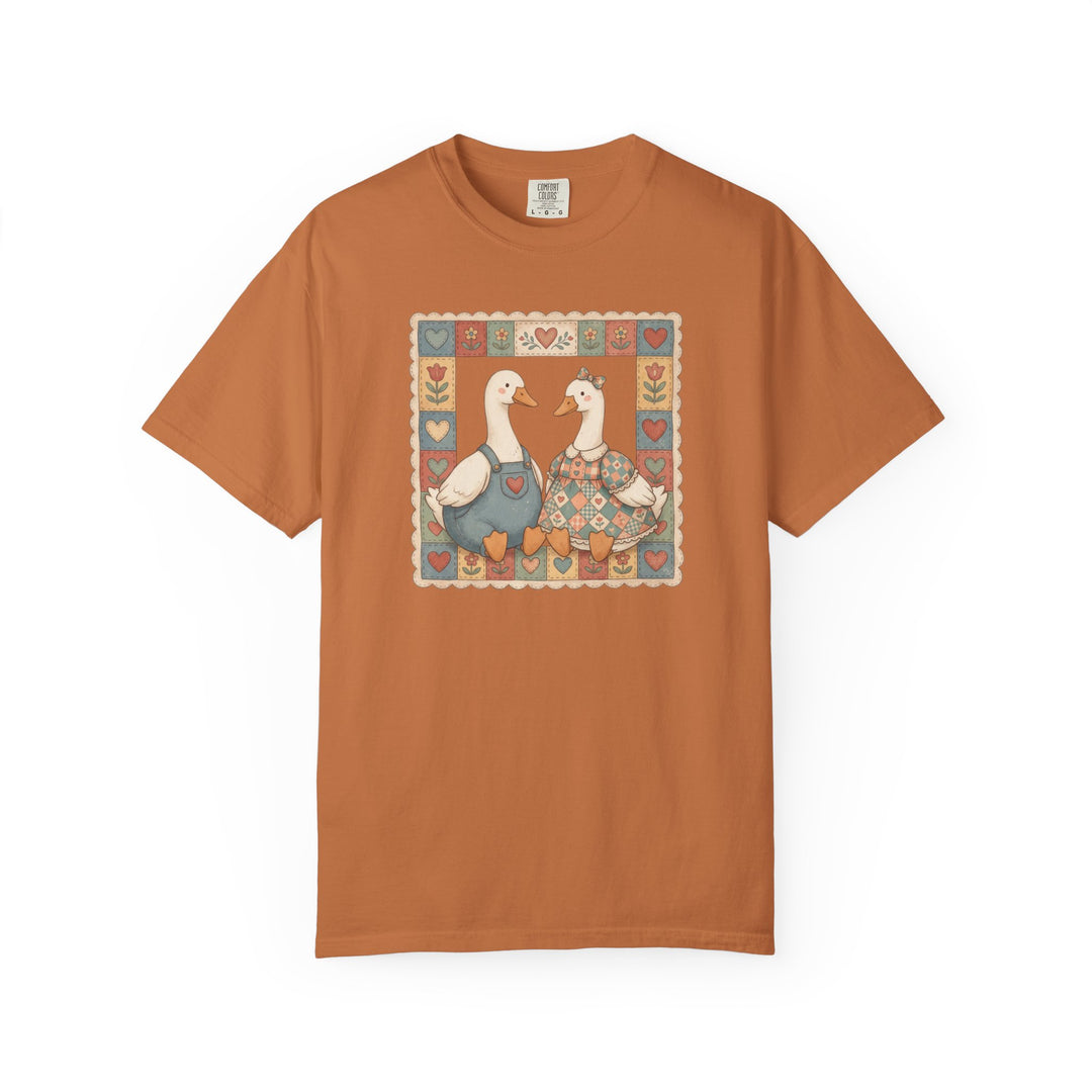 Thrifted Geese Tee features two geese in folk-art attire framed by a quilt-style border on a rust-orange Comfort Colors shirt, offering cozy, durable wear.