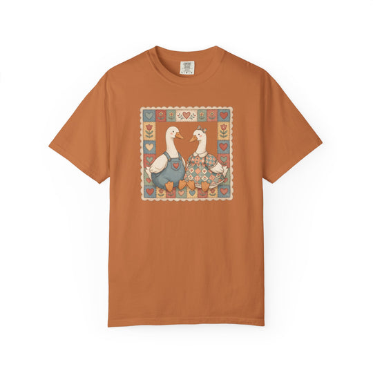 Thrifted Geese Tee features two geese in folk-art attire framed by a quilt-style border on a rust-orange Comfort Colors shirt, offering cozy, durable wear.