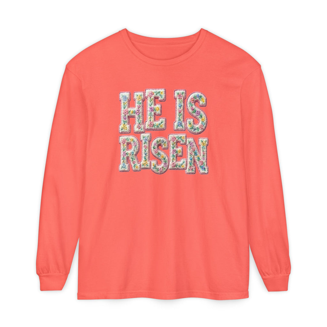Coral long-sleeve tee with HE IS RISEN in pastel floral print, reflecting Easter themes. Made of 100% ring-spun cotton for comfort.