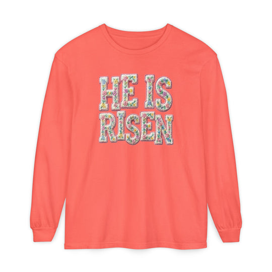 Coral long-sleeve tee with HE IS RISEN in pastel floral print, reflecting Easter themes. Made of 100% ring-spun cotton for comfort.