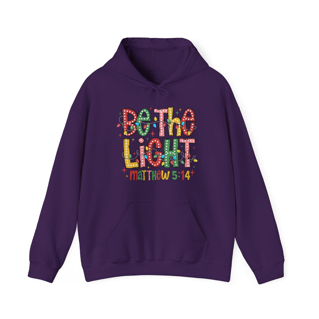 Purple 'Be the Light' hoodie with festive graphic and Bible verse, featuring a kangaroo pocket and drawstring hood, offering comfort and warmth.