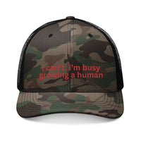 Camouflage-patterned trucker hat with mesh back, embroidered with i can’t. i’m busy growing a human. in red, from Faith Family Designs.