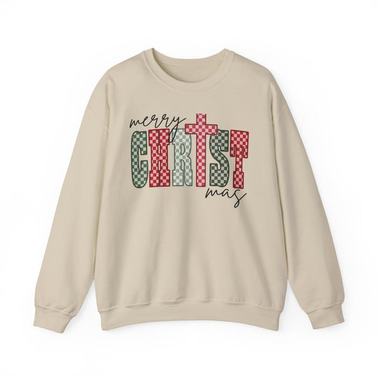 Cream-colored crewneck sweatshirt with merry CHRISTmas graphic in red and green checkerboard and script fonts, featuring a cross. Cozy, durable blend, ideal for colder months.