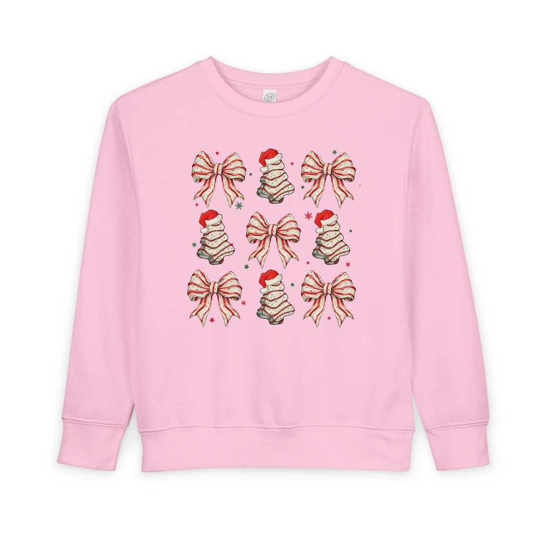 Light-pink toddler sweatshirt with holiday-themed motifs in a 3×3 grid, featuring bows, frosting swirls with Santa hats, and scattered stars. Cozy, durable fabric.