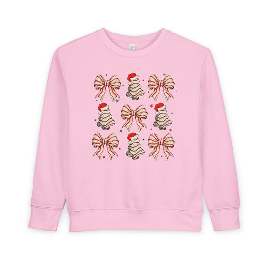 Light-pink toddler sweatshirt with holiday-themed motifs in a 3×3 grid, featuring bows, frosting swirls with Santa hats, and scattered stars. Cozy, durable fabric.