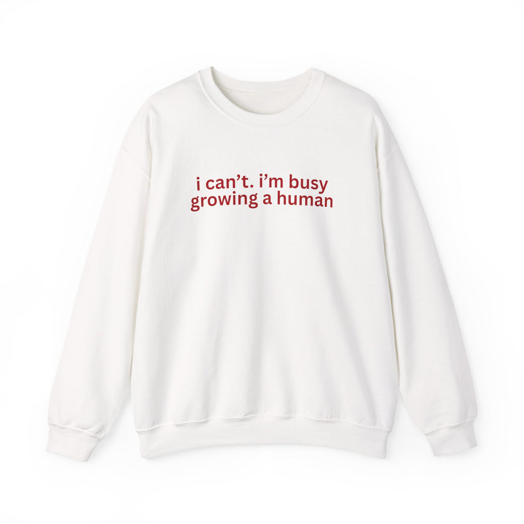 White crewneck sweatshirt with red text: “i can’t. i’m busy growing a human.” Features ribbed knit collar and durable stitching. Cozy, unisex fit from Faith Family Designs.