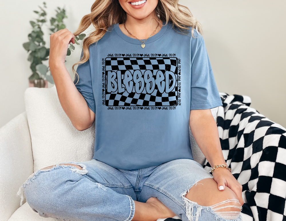 Woman wearing the Blessed Tee, a classic unisex jersey short sleeve, sitting casually on a chair, showcasing its comfortable fit and soft cotton fabric.