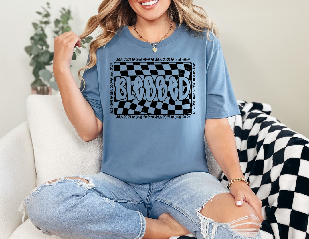 Woman wearing the Blessed Tee, a classic unisex jersey short sleeve, sitting casually on a chair, showcasing its comfortable fit and soft cotton fabric.