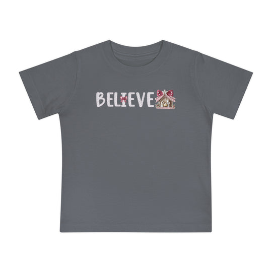 Believe Baby Tee: Slate gray children's T-shirt with BELIEVE in white, featuring a pink-bowed I and gingerbread-style Christmas stable, perfect for stylish first steps.