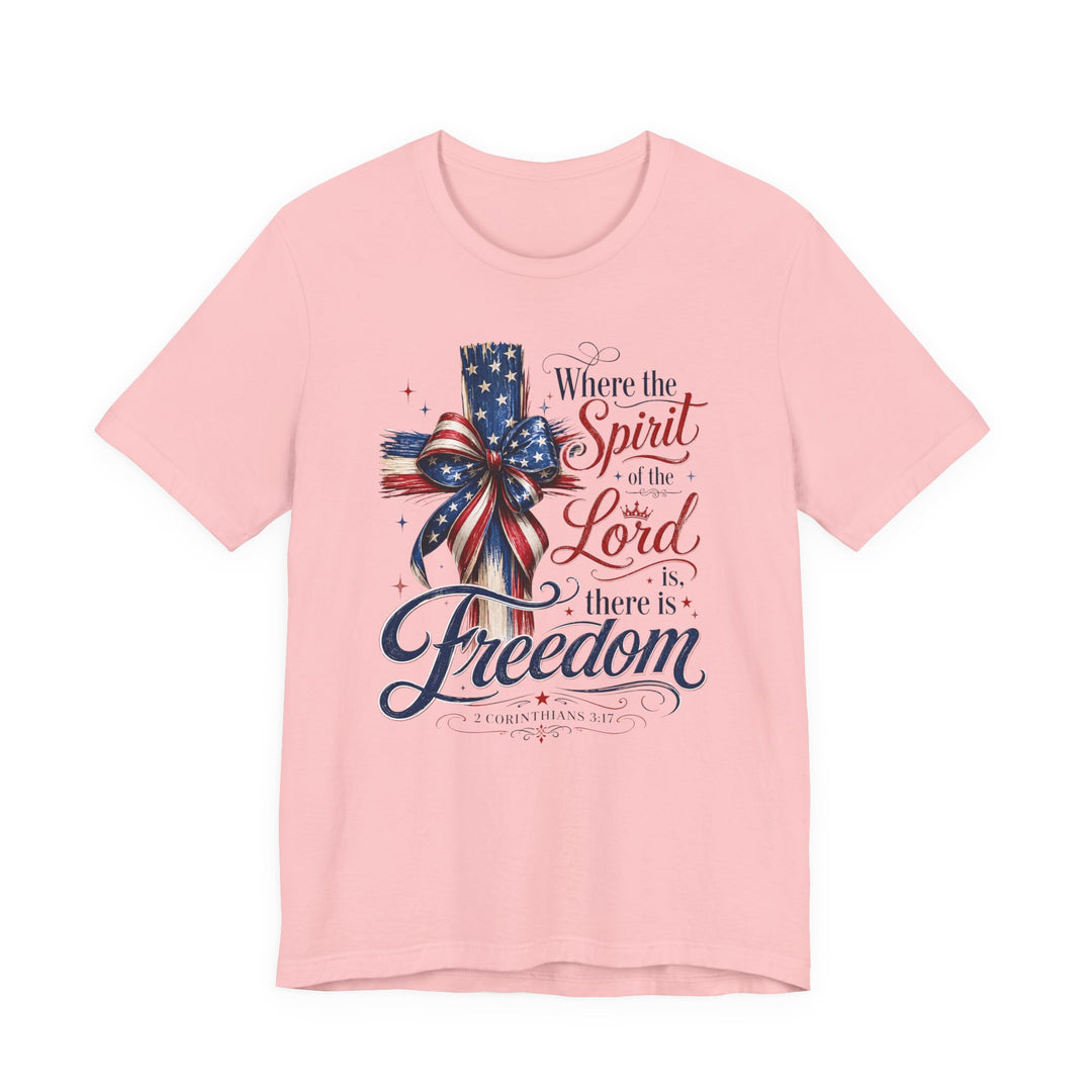 Spirit of the Lord Tee featuring a wooden cross with a stars-and-stripes bow and 2 Corinthians 3:17 verse in red and blue script on pale-pink fabric.