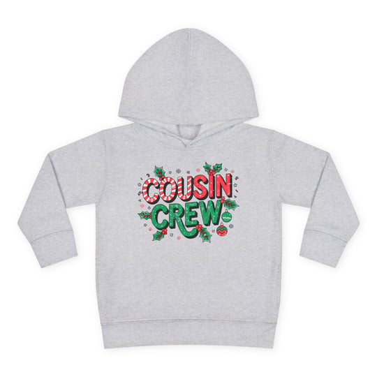 Cousin Crew Christmas Toddler Hoodie with holiday-themed graphics, COUSIN CREW text, holly, snowflakes, ornaments; designed for comfort with jersey-lined hood and side seam pockets.