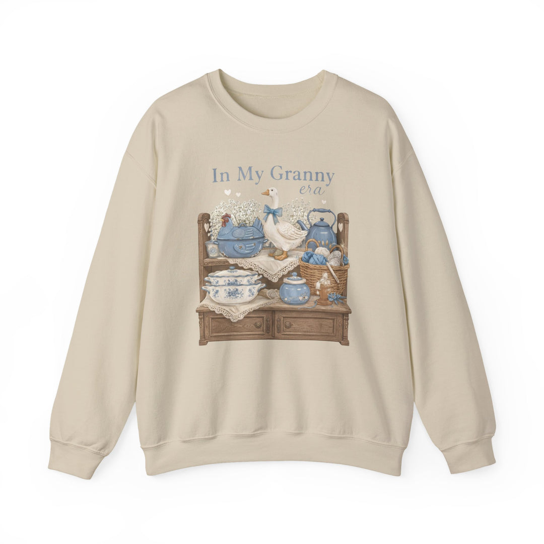 Light-beige In My Granny Era crewneck sweatshirt with vintage-style print featuring a sideboard, ceramic goose, floral teapot set, yarn basket, and baby’s-breath flowers.